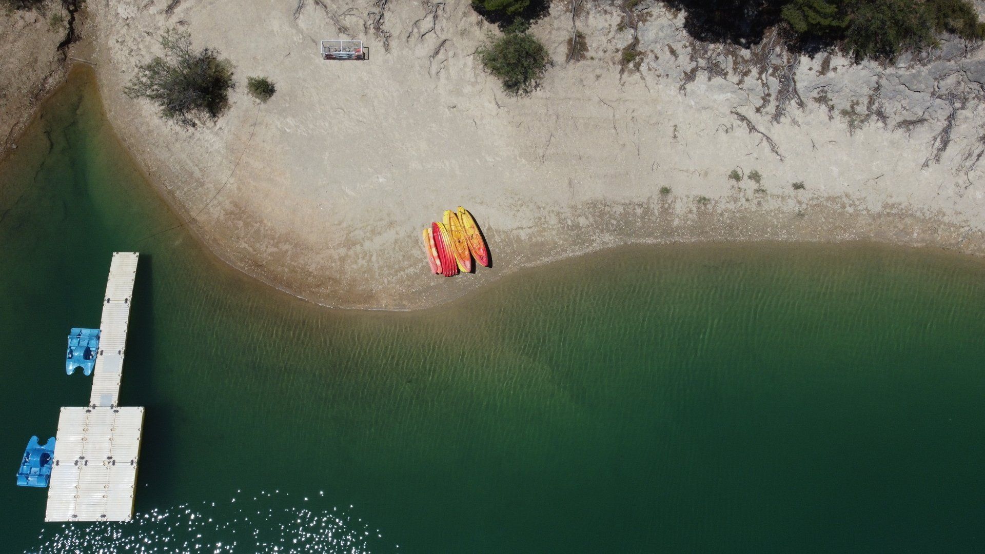 Vista aérea de una playa con kayaks y un muelle sobre agua turquesa.