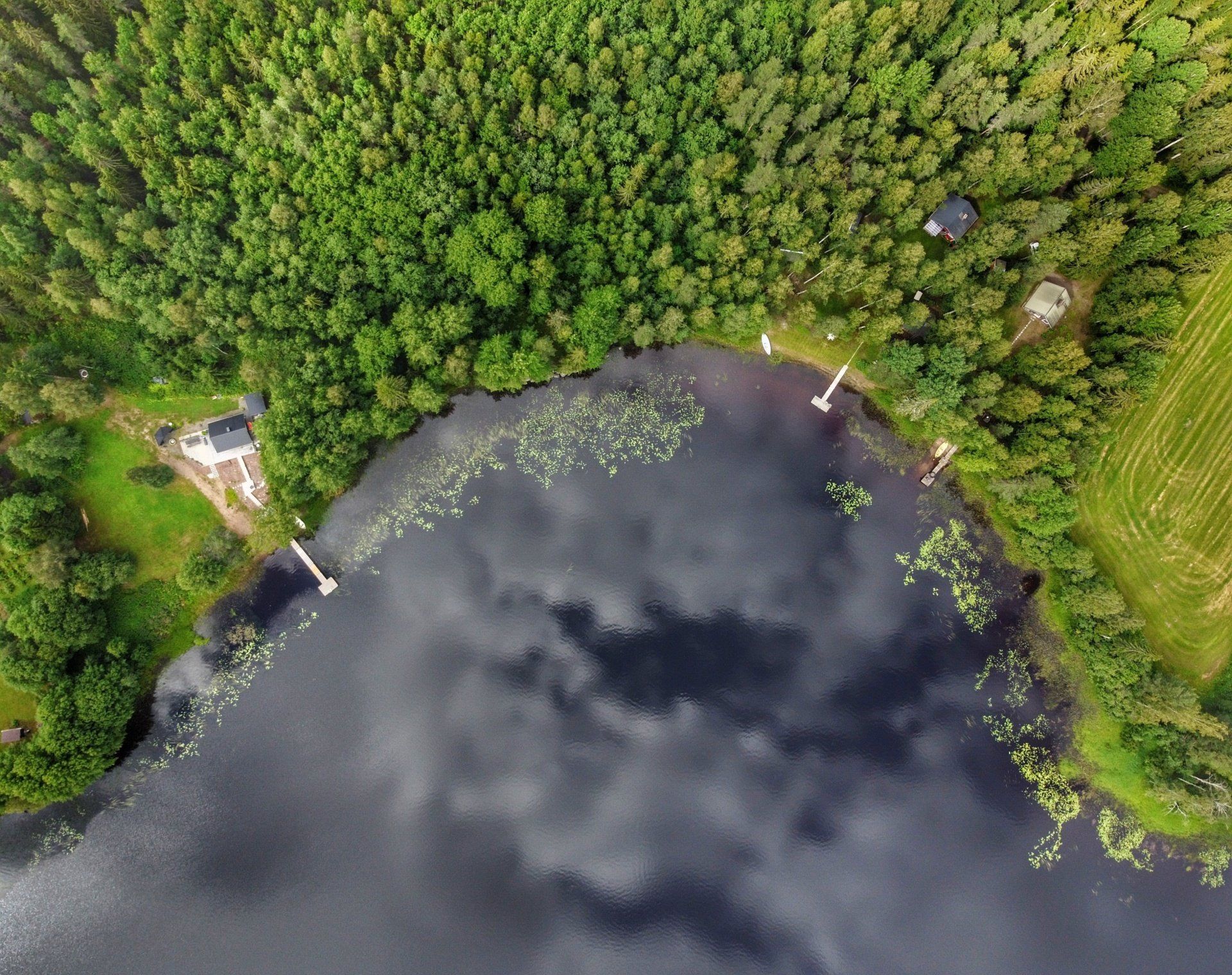 Vista aérea de un lago, orilla boscosa con pequeños muelles y un cielo parcialmente nublado reflejándose en el agua.