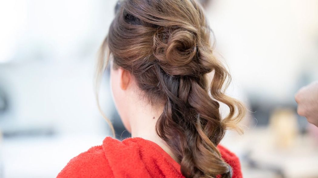 Mujer con cabello castaño rizado recogido, con un top rojo y peinada.