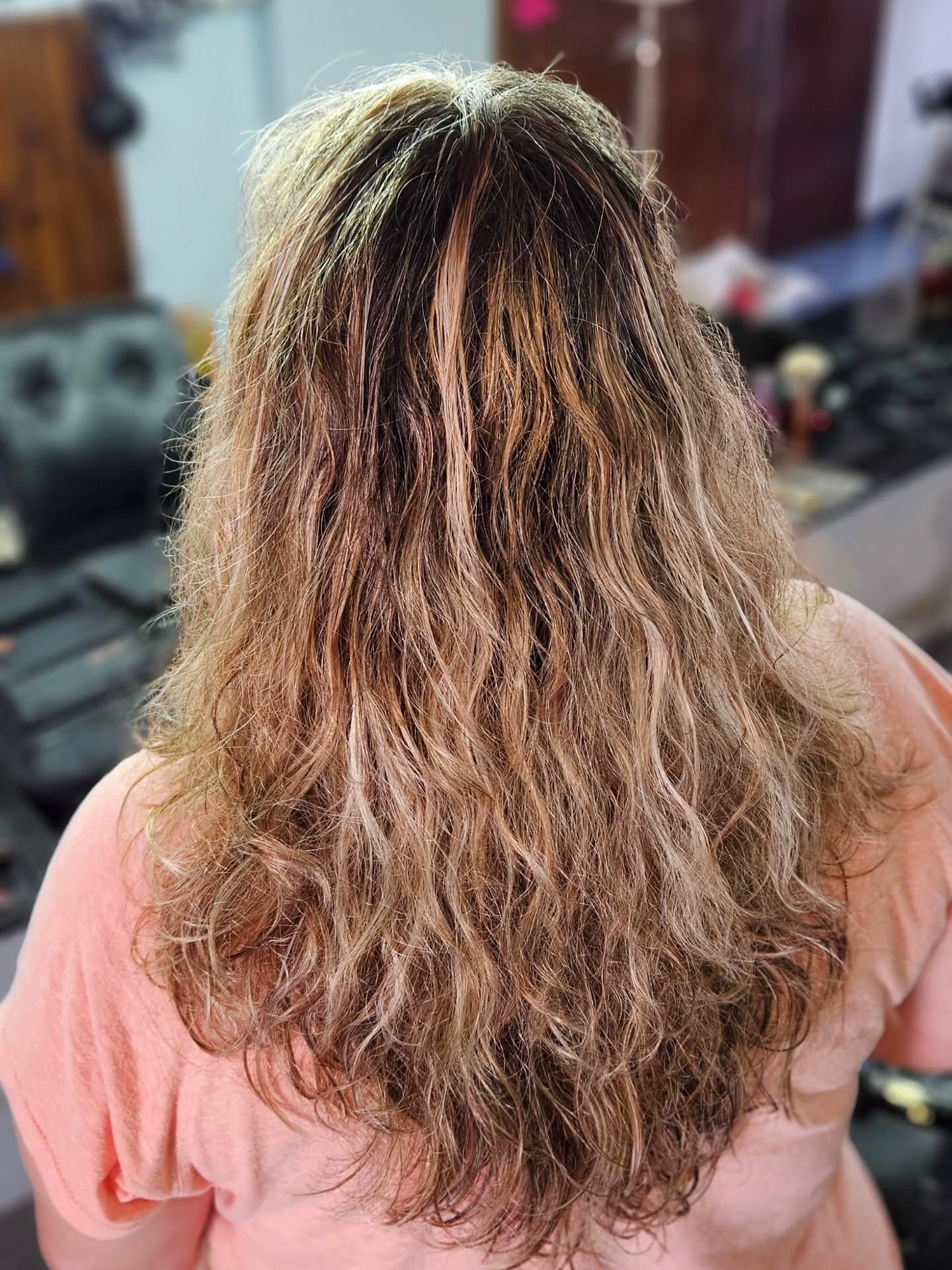 Mujer con cabello rubio ondulado y multicolor, vista desde atrás. Lleva una blusa color melocotón.