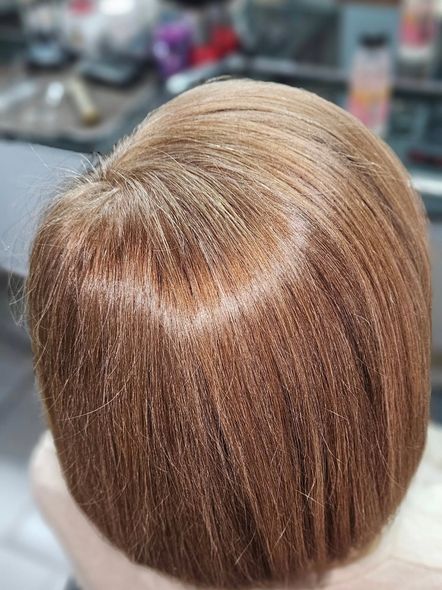 Primer plano de la cabeza de una persona con cabello castaño claro, liso y largo hasta los hombros, en un salón de belleza.