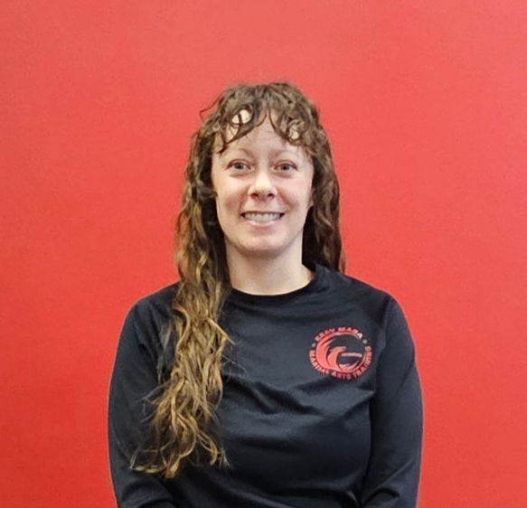 Woman with curly hair in a black shirt smiles in front of a red wall.