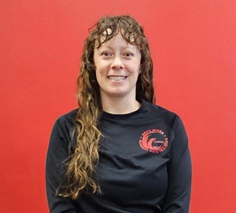 Woman with curly hair in a black shirt smiles in front of a red wall.