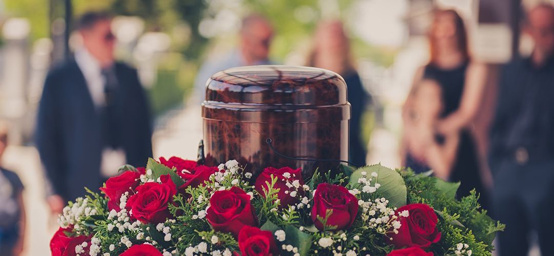 a urn surrounded by red roses and baby 's breath is on a coffin at a funeral .