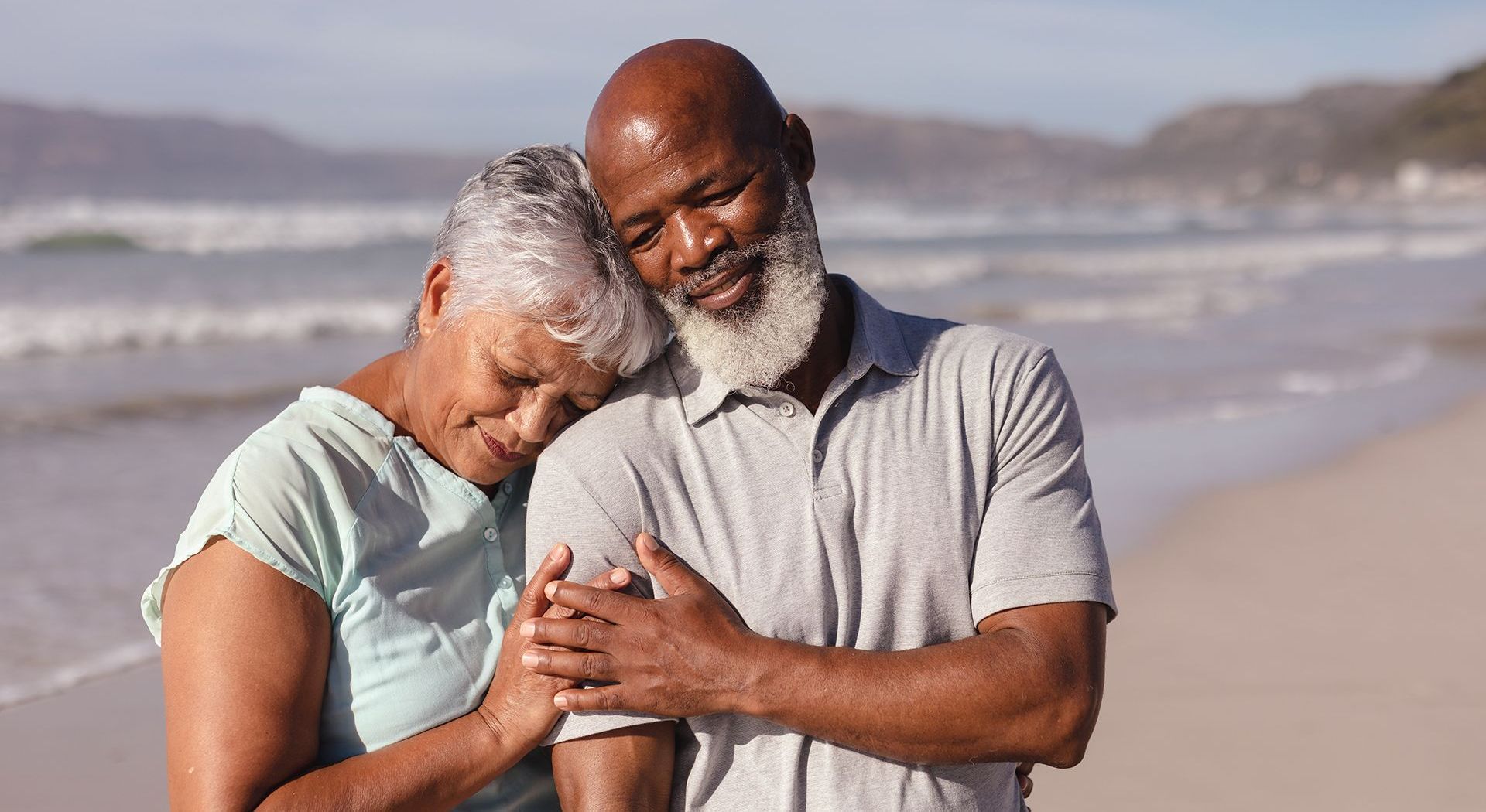 an elderly couple is hugging each other on the beach .
