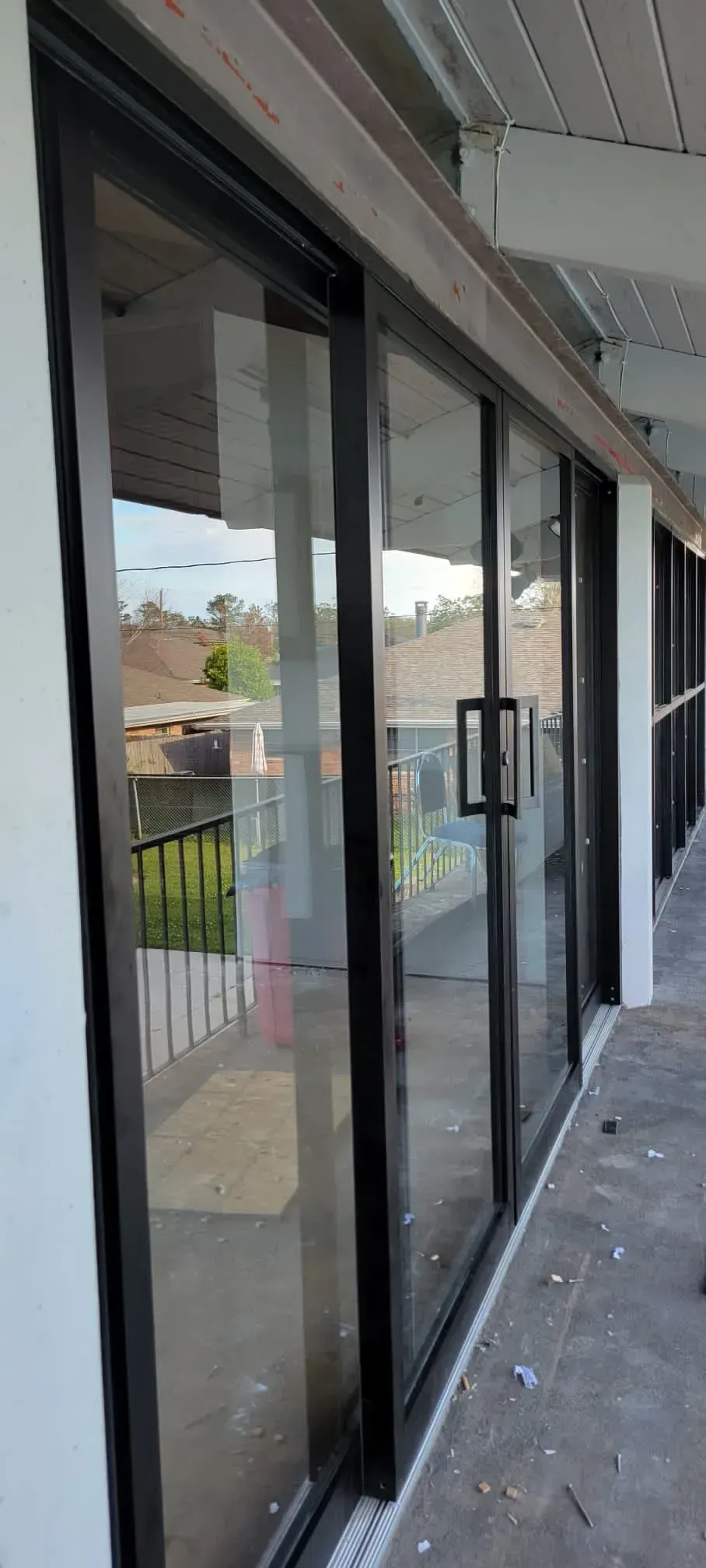 Black-framed glass sliding doors on a concrete patio, reflecting the outdoors.