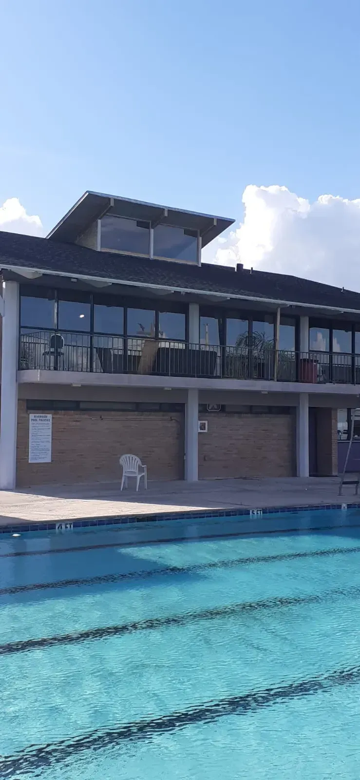 Swimming pool next to a two-story building with large windows and a dark roof under a blue sky.