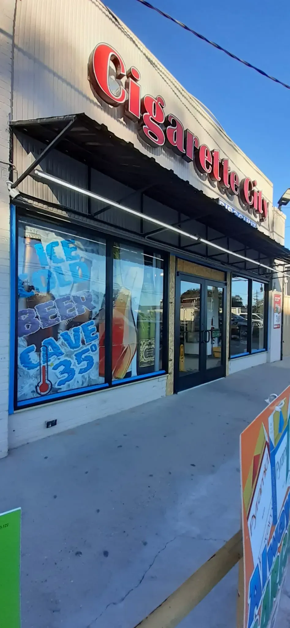 A store with a black awning and large windows. The sign says “Cigarettes.” There are colorful window displays.