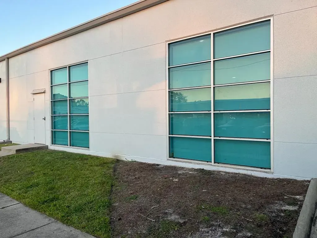 White building with two large windows reflecting blue sky and trees; small patch of grass in front.