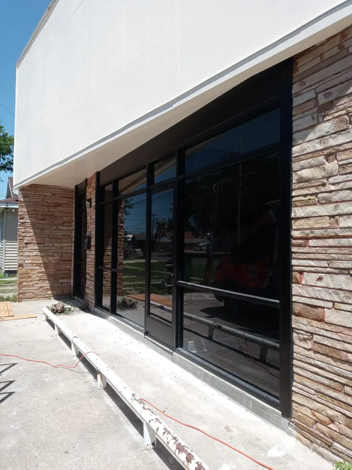 Exterior of a building with black-framed windows and stone facade. A concrete ramp leads to the entrance.