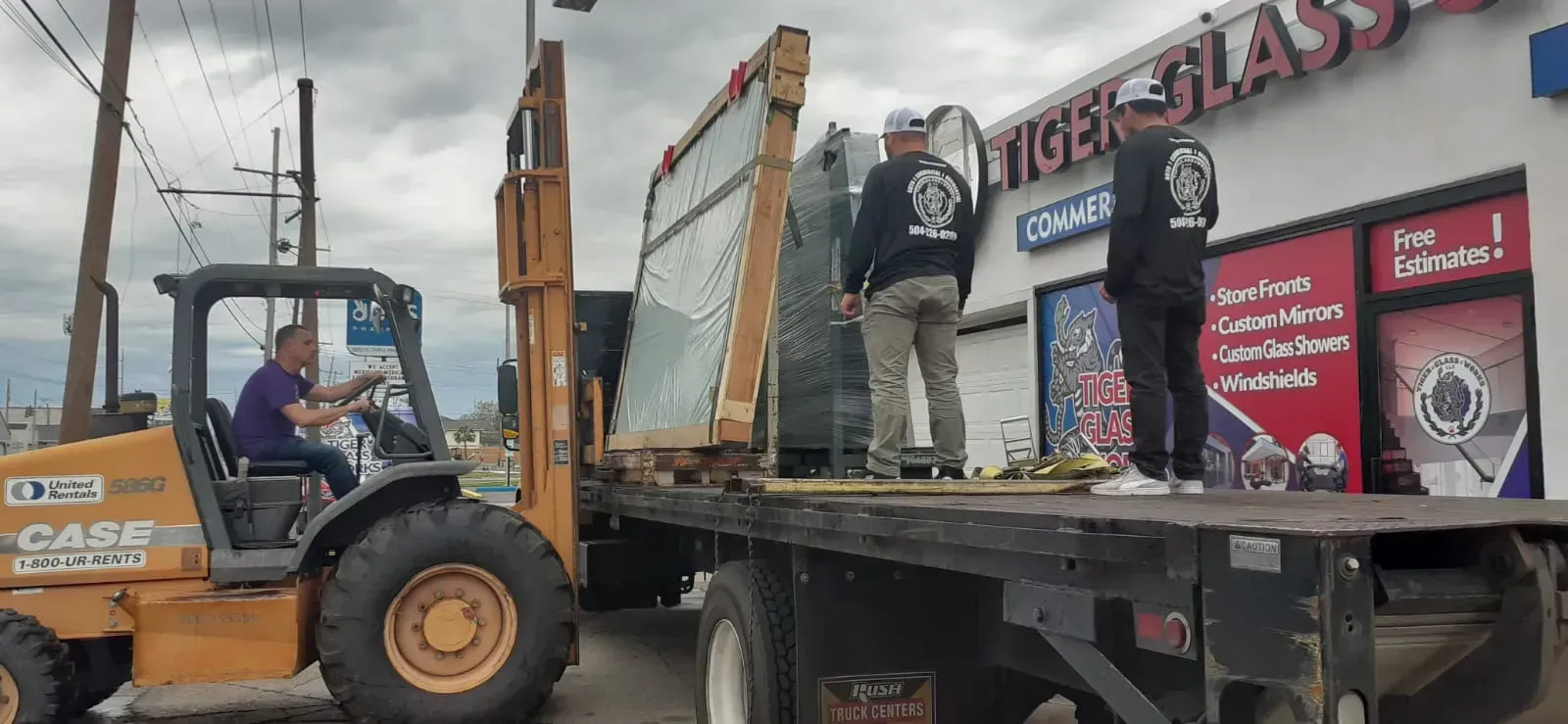 A forklift operator loads glass onto a flatbed truck at Tiger Glass. Two men stand on the truck, wearing black shirts.