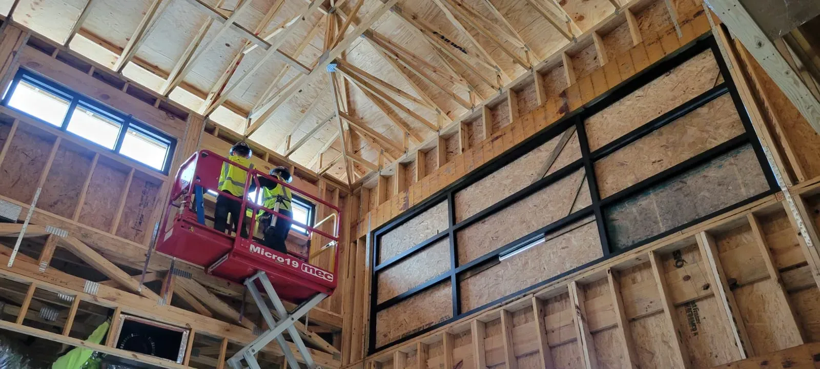 Construction workers on a lift, installing a window frame in a building under construction.  