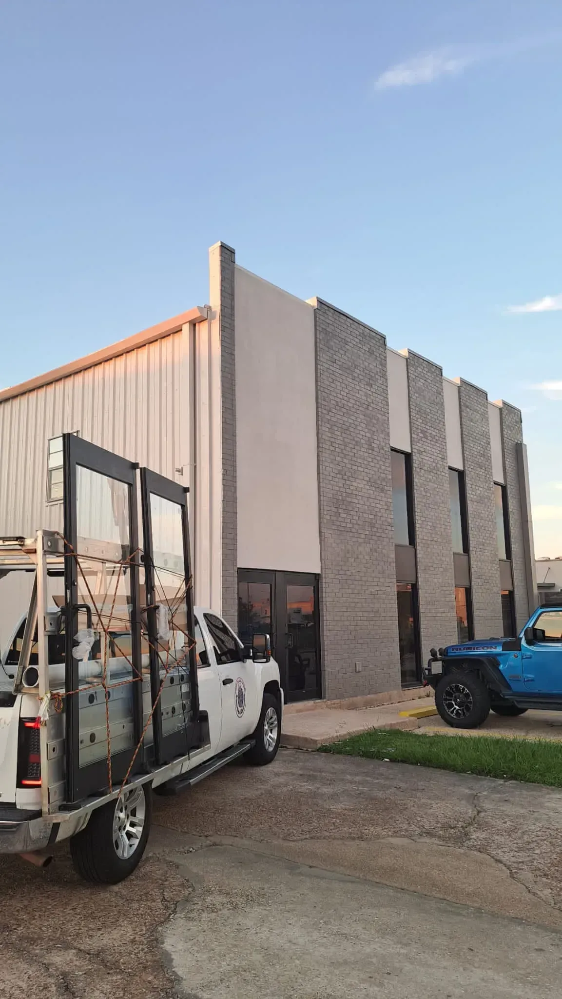 Truck with glass panels parked outside a modern building with gray brick facade under a blue sky.