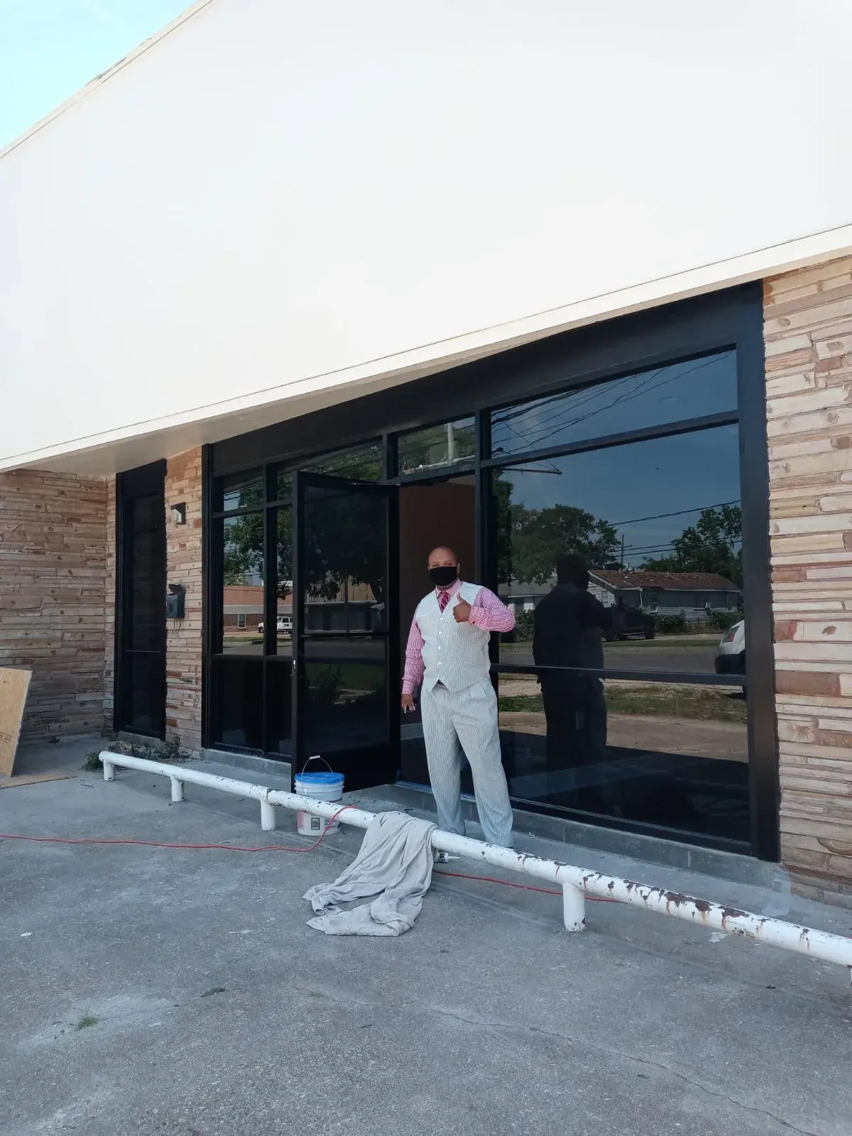 Person in vest stands by a building with tinted windows. The building has a white top and brick sides.