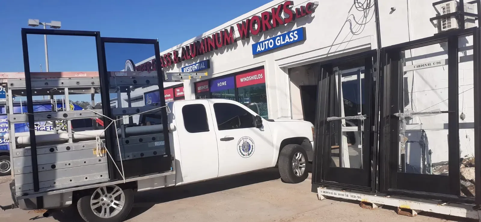 A white truck carrying large glass doors parked in front of a glass store.