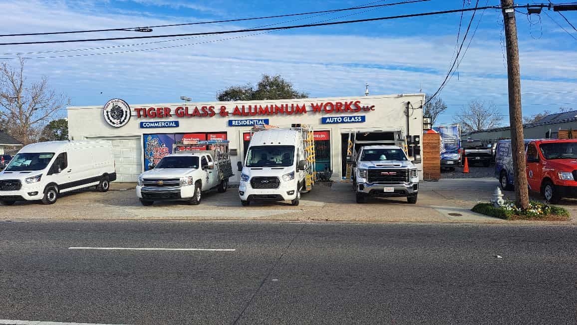 Tiger Glass & Aluminum Works storefront with multiple work vans parked in front on a sunny day.
