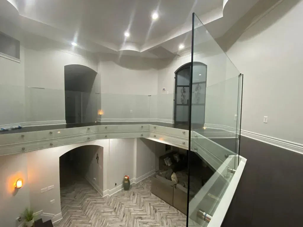 Interior view: modern home with glass railings, arched doorways, dark wood floors, and recessed lighting.