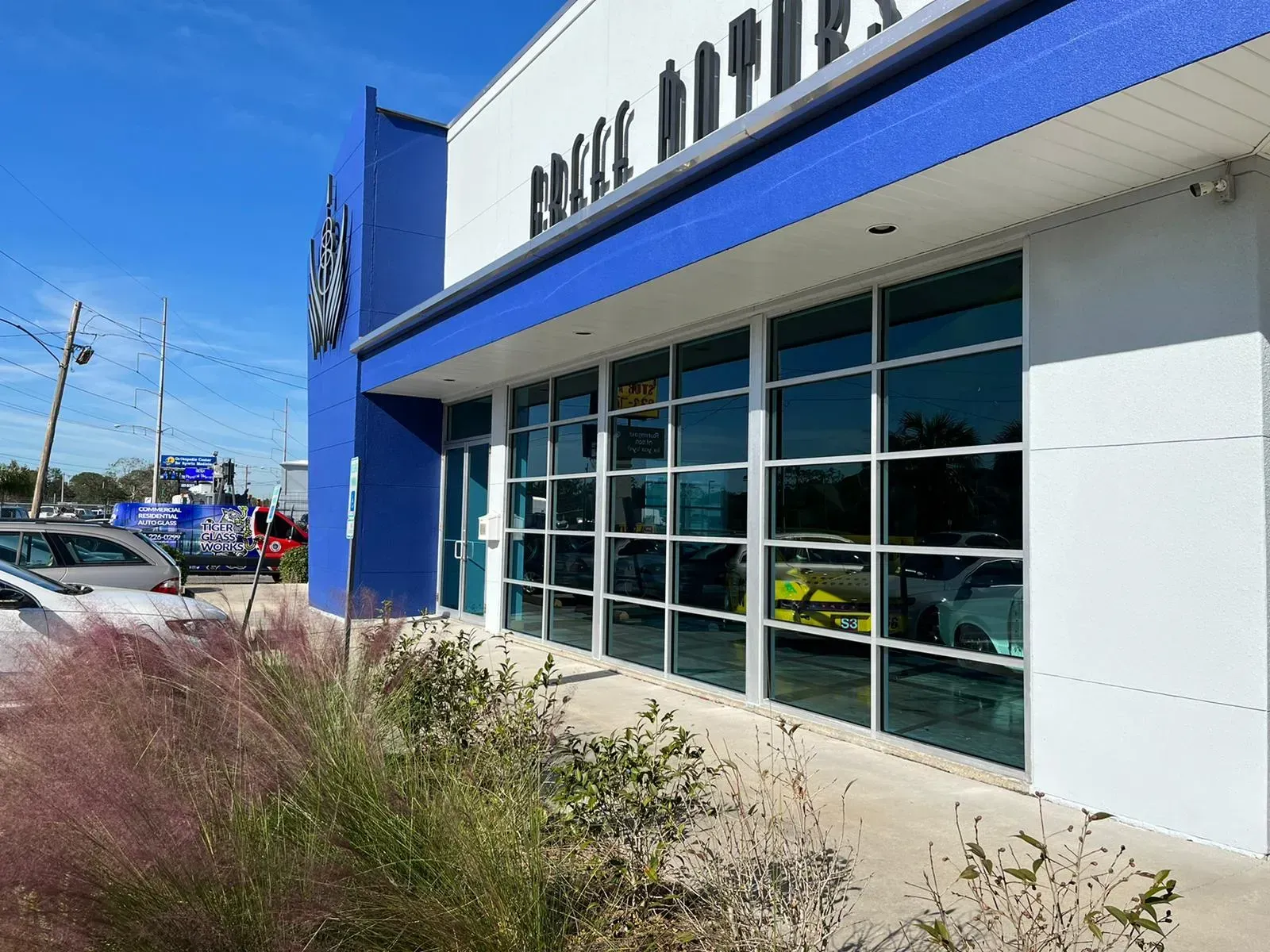 Exterior view of a car dealership with blue and white accents, featuring large windows and parked cars outside.