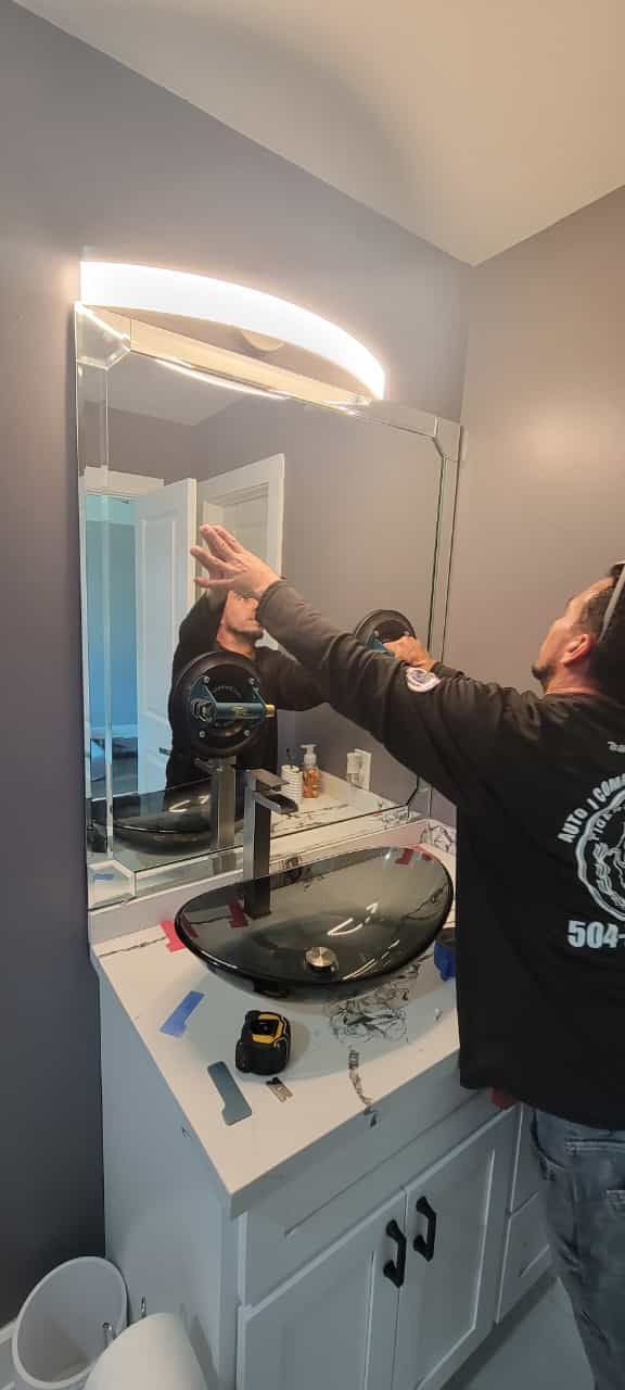 A person installs a lighted mirror above a bathroom vanity.