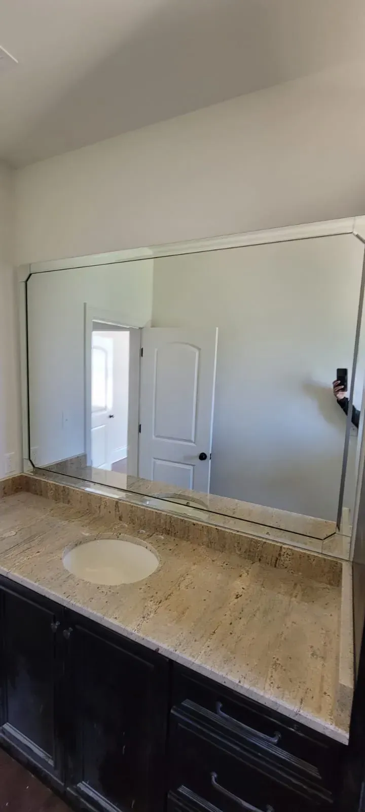 Bathroom vanity with a large mirror, granite countertop, and black cabinets. A doorway is reflected in the mirror.