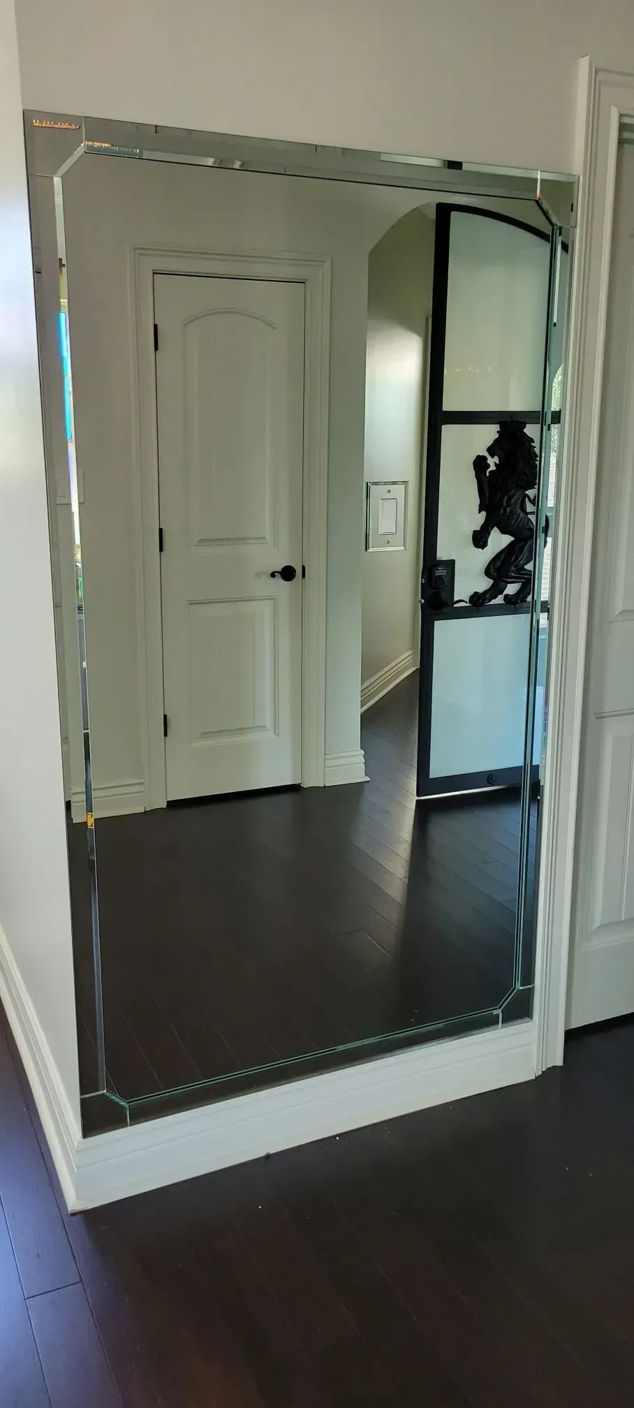 Large rectangular mirror on a wall reflecting a hallway with white doors and dark wood floors.