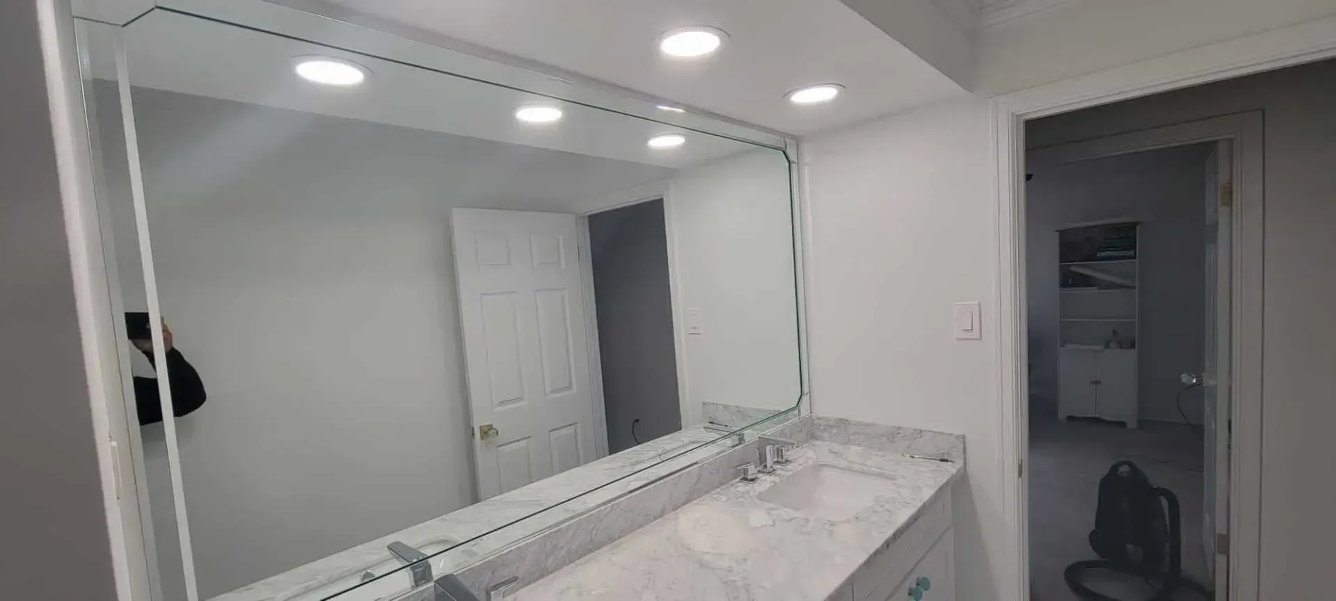 Bathroom with a large mirror, vanity, and recessed lighting. A door leads to another room.