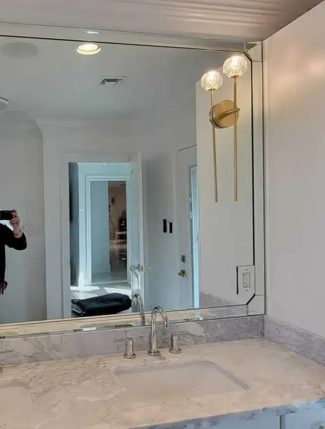 Bathroom with a large mirror, sink, and modern gold sconce.