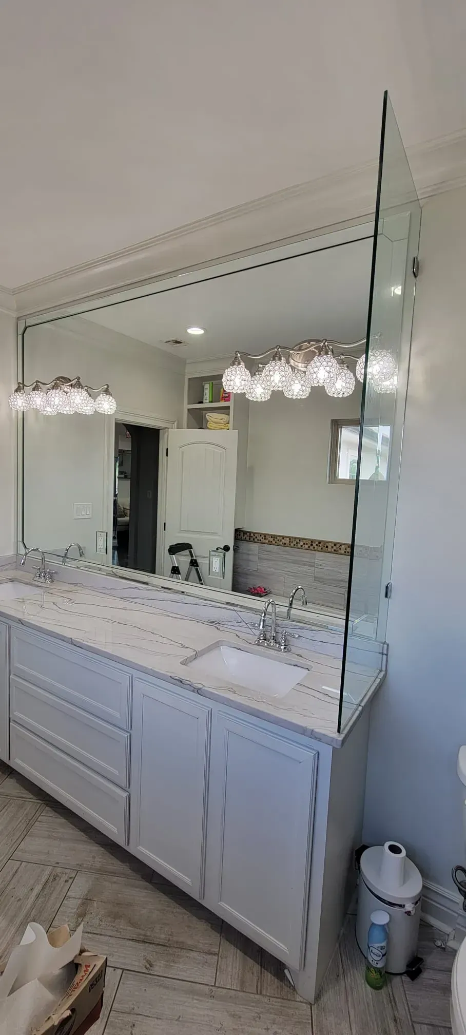 A modern bathroom with a large mirror and double vanity. White cabinets, marble countertop, and pendant lights.