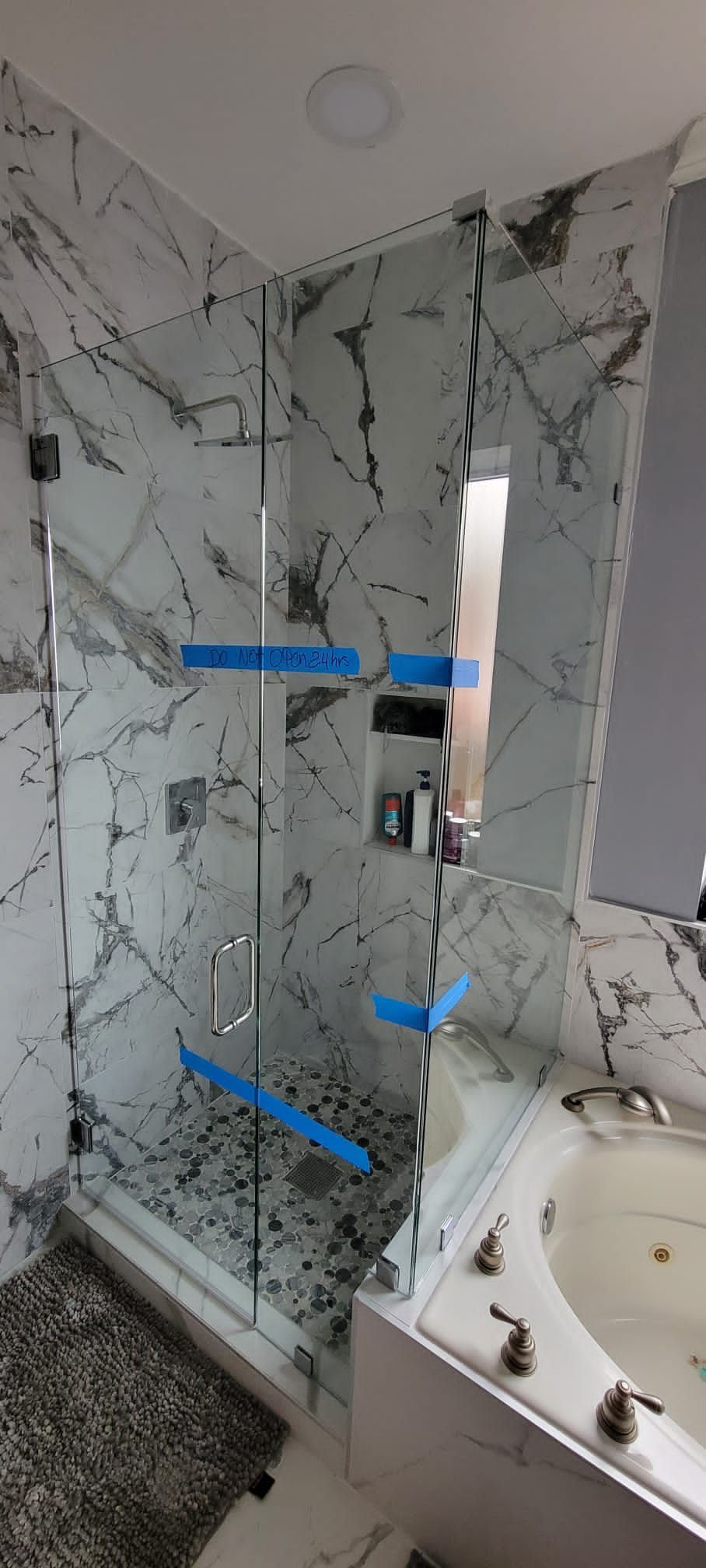 A corner shower with glass panels and a marble patterned wall is visible next to a bathtub.