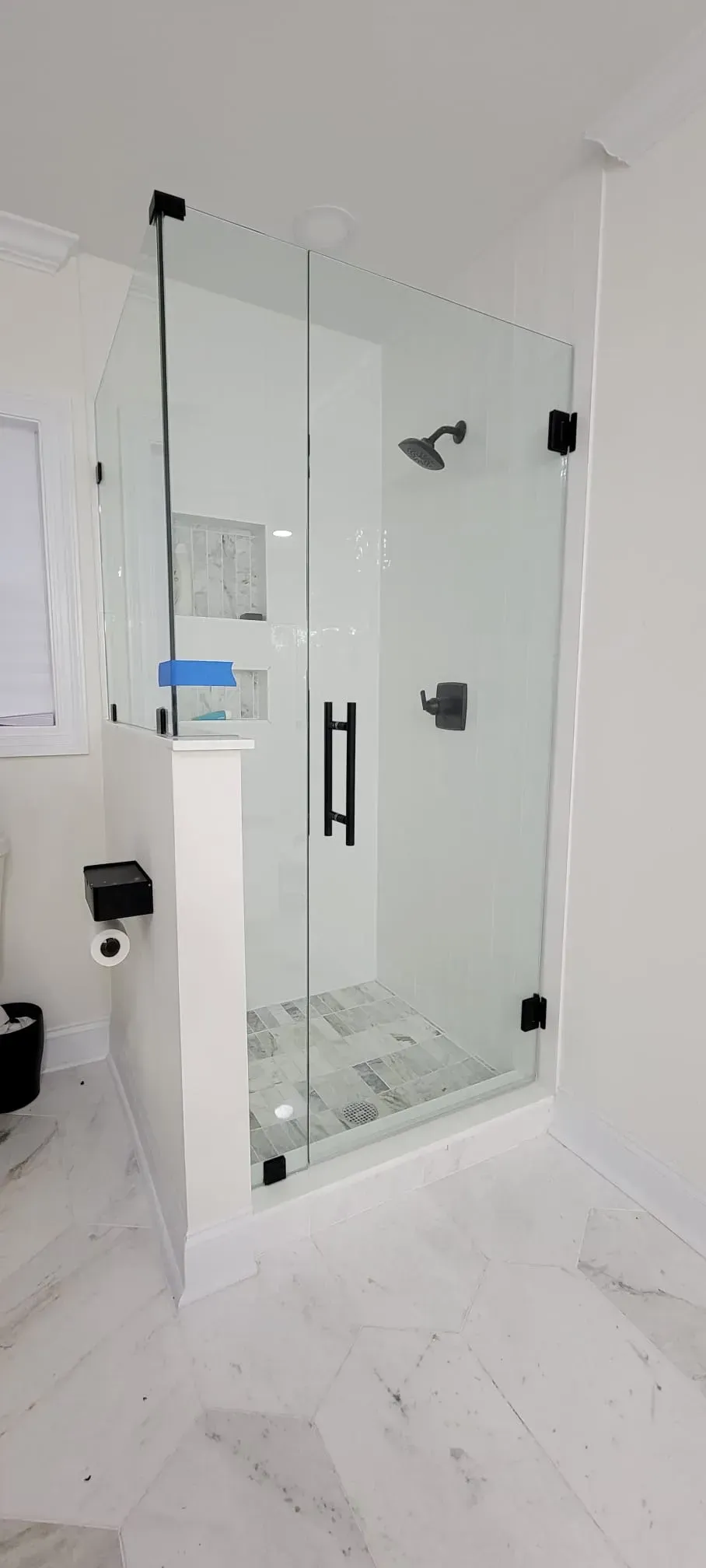 Modern shower enclosure with black hardware, white walls, and marble flooring.