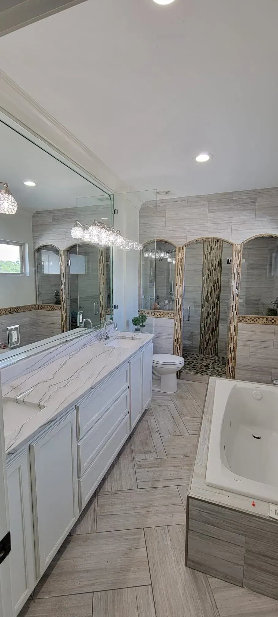 Bathroom with white cabinets, large mirror, toilet, and a bathtub with tile accents.