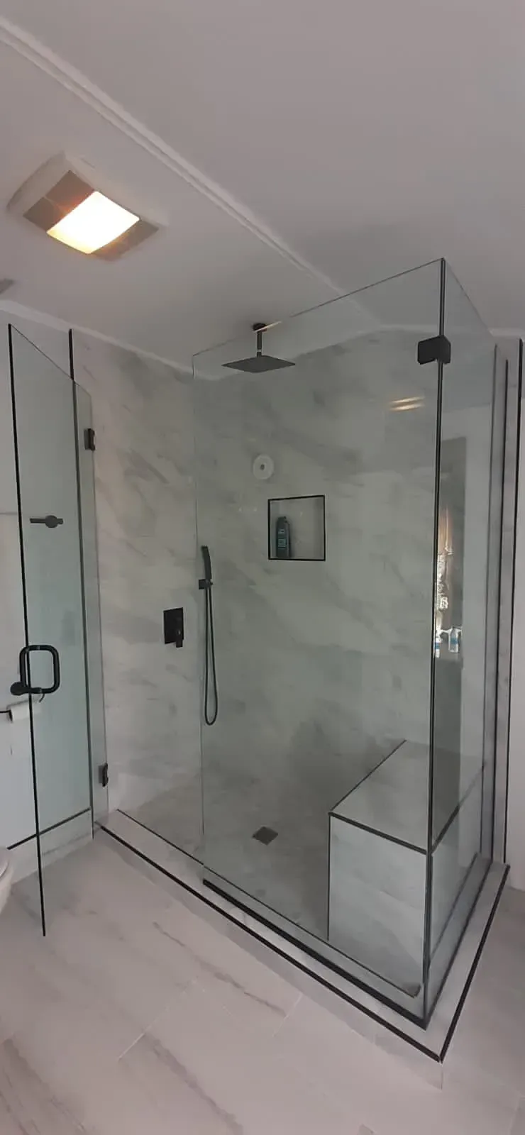 Modern shower with marble walls, glass doors, black fixtures, and a built-in bench.