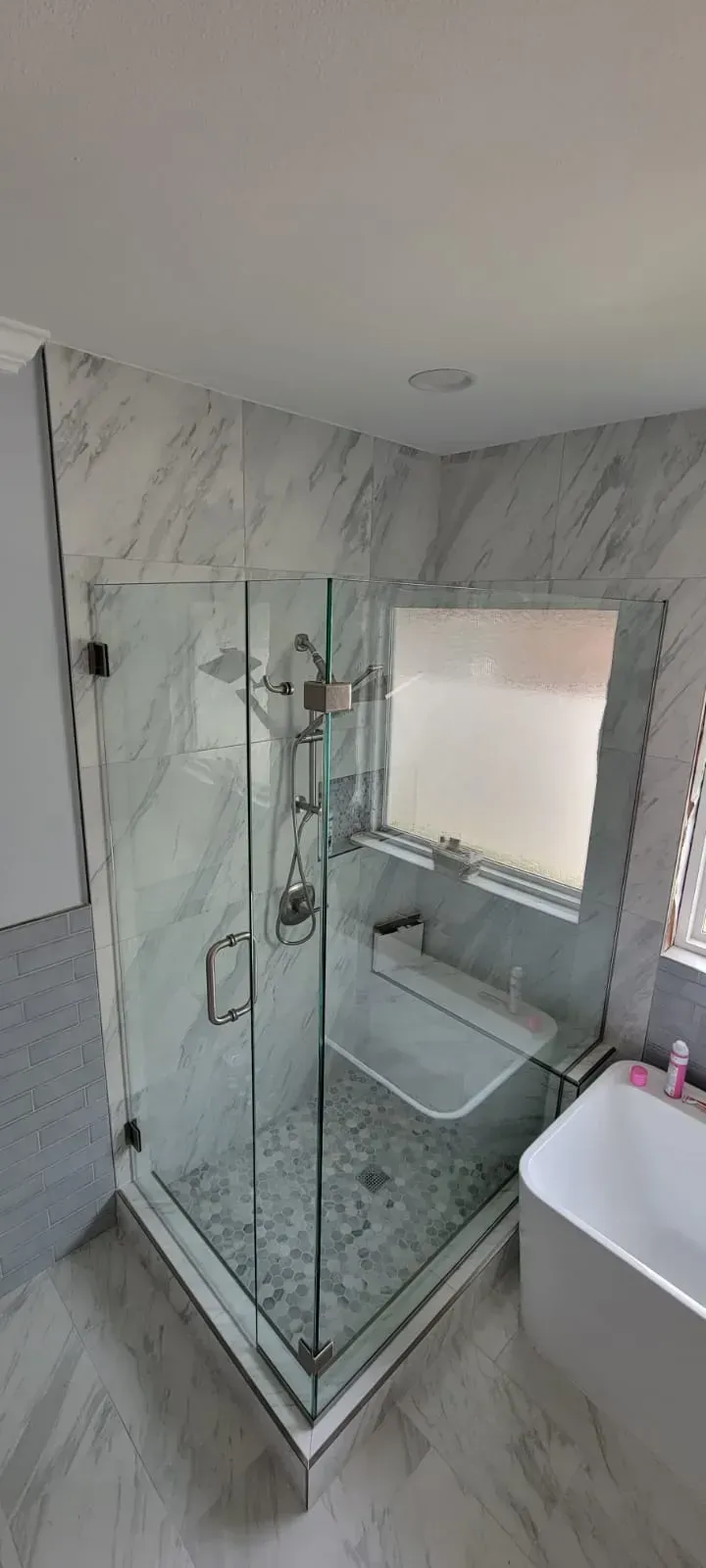 Modern bathroom with a glass shower, white walls, and a window.