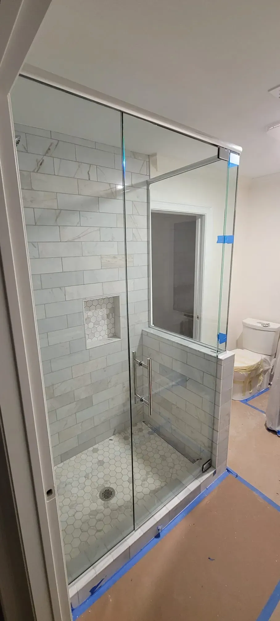 Glass shower enclosure with white tile walls and a built-in shelf.