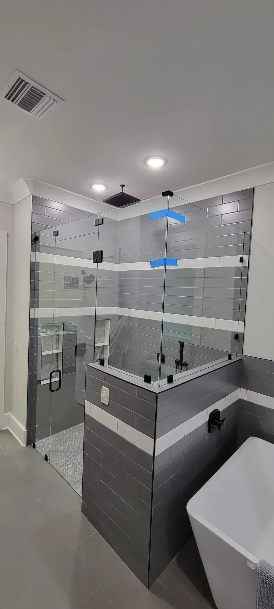 Modern shower with glass doors, black showerhead, and gray tile walls and floor.