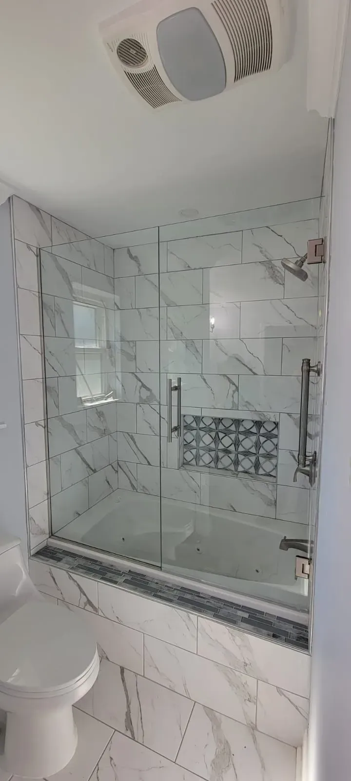 A bathroom with marble tile and a glass shower door.