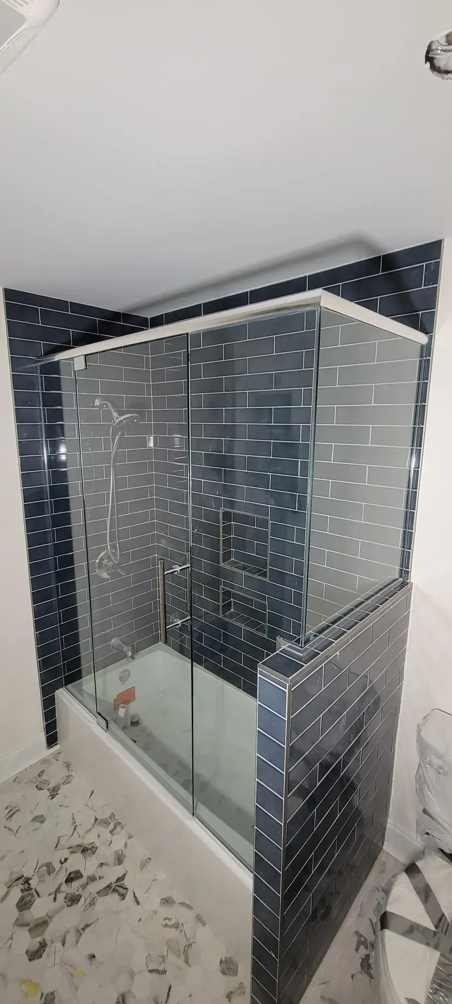 A bathroom with a bathtub, glass shower doors, and dark blue tile.