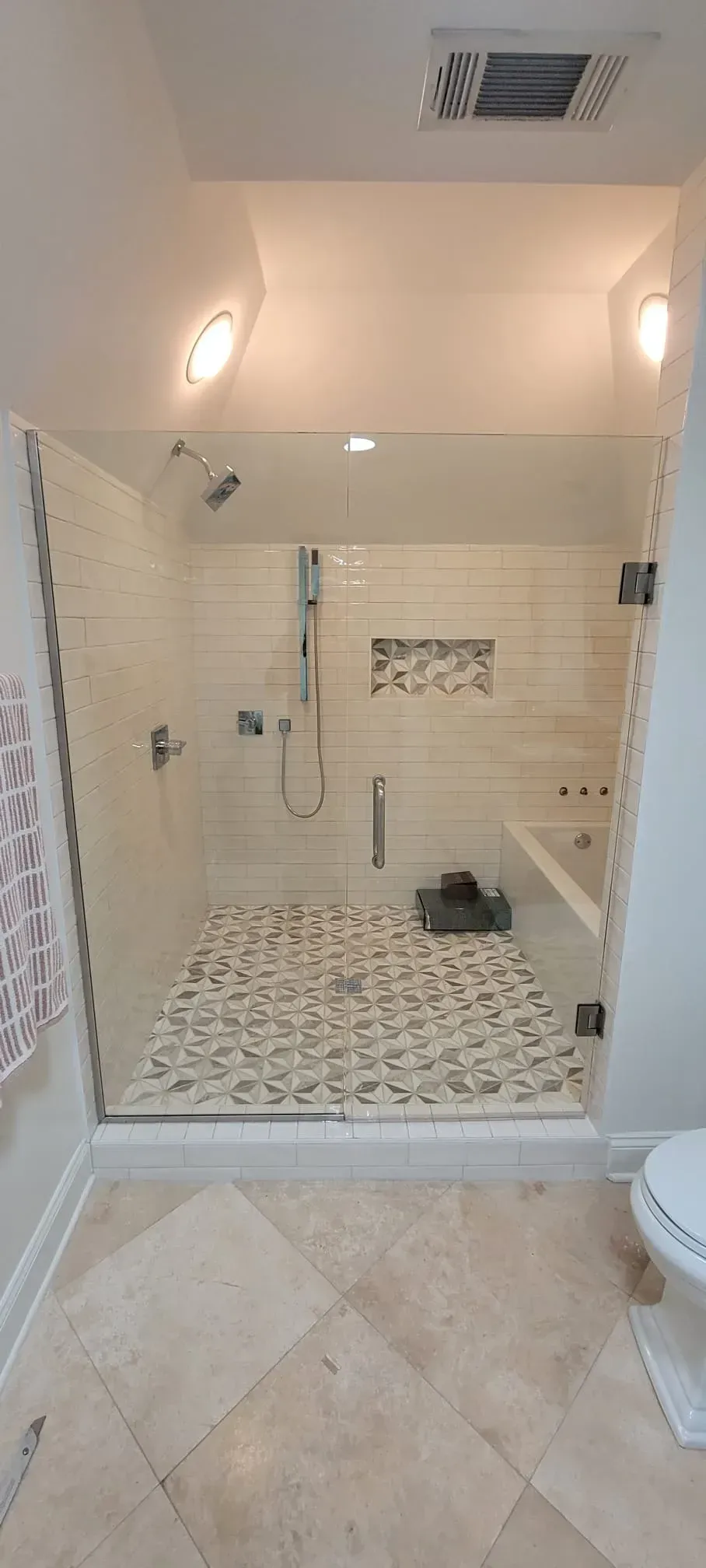 A modern bathroom with a glass-enclosed shower, featuring pebble tile flooring and a white tile wall.