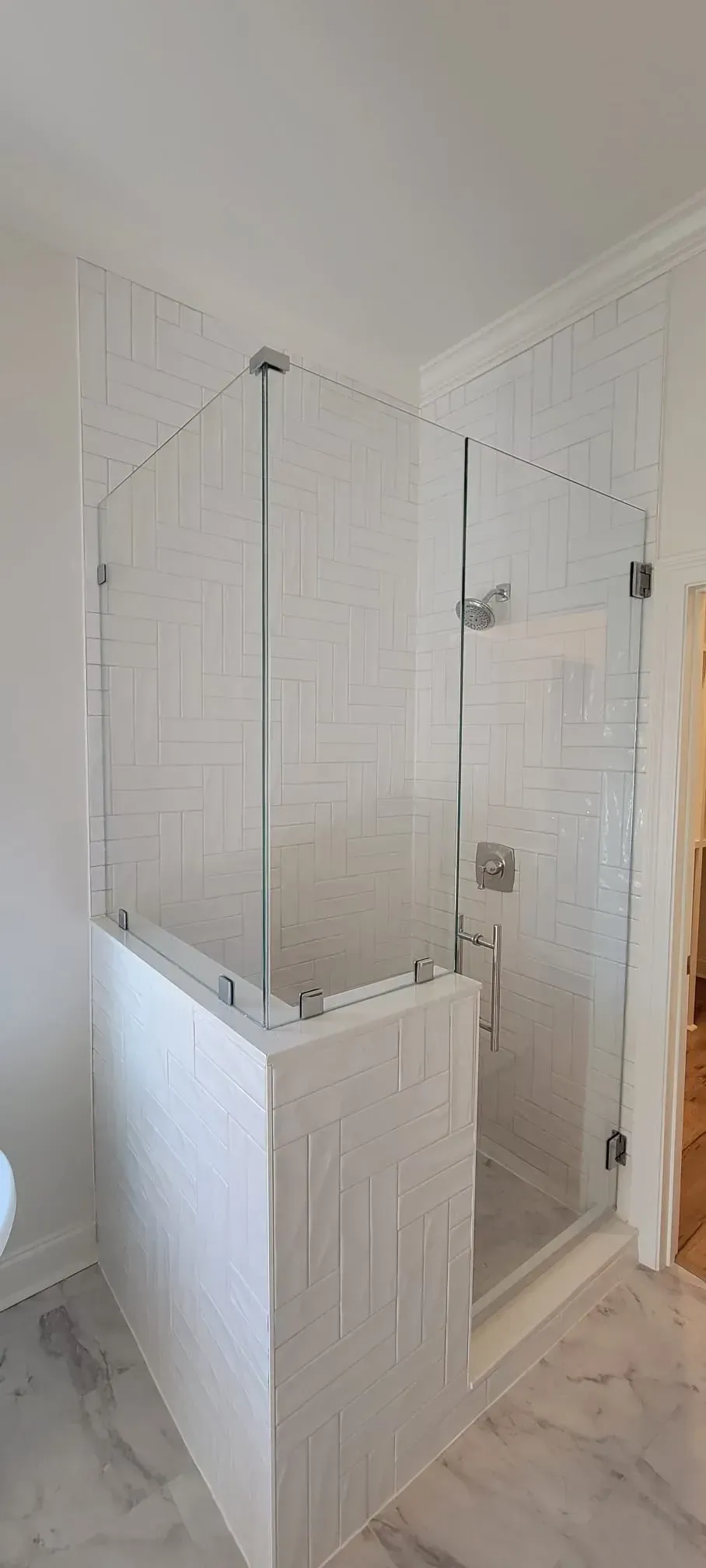Modern walk-in shower with clear glass panels and white tiled walls.