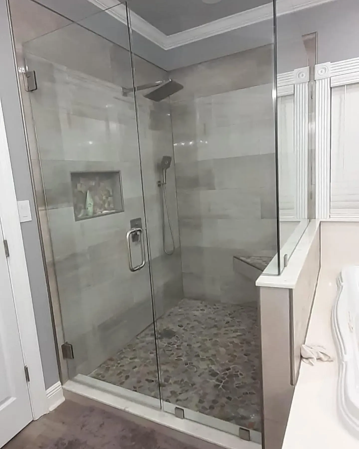 Glass shower enclosure with gray tiled walls, pebble floor, and chrome fixtures.