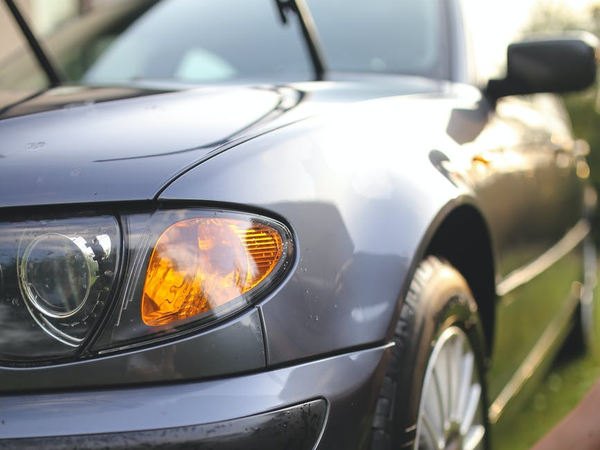 Gray car being washed, close up on headlight and tire in sunlight.