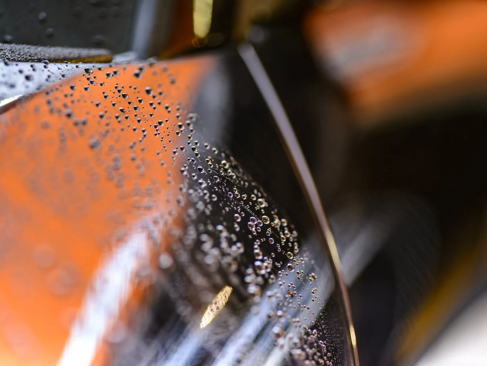 Black car surface with water droplets, orange reflection visible.