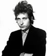 Bob Dylan in a black suit, staring intently. He has curly, messy hair.