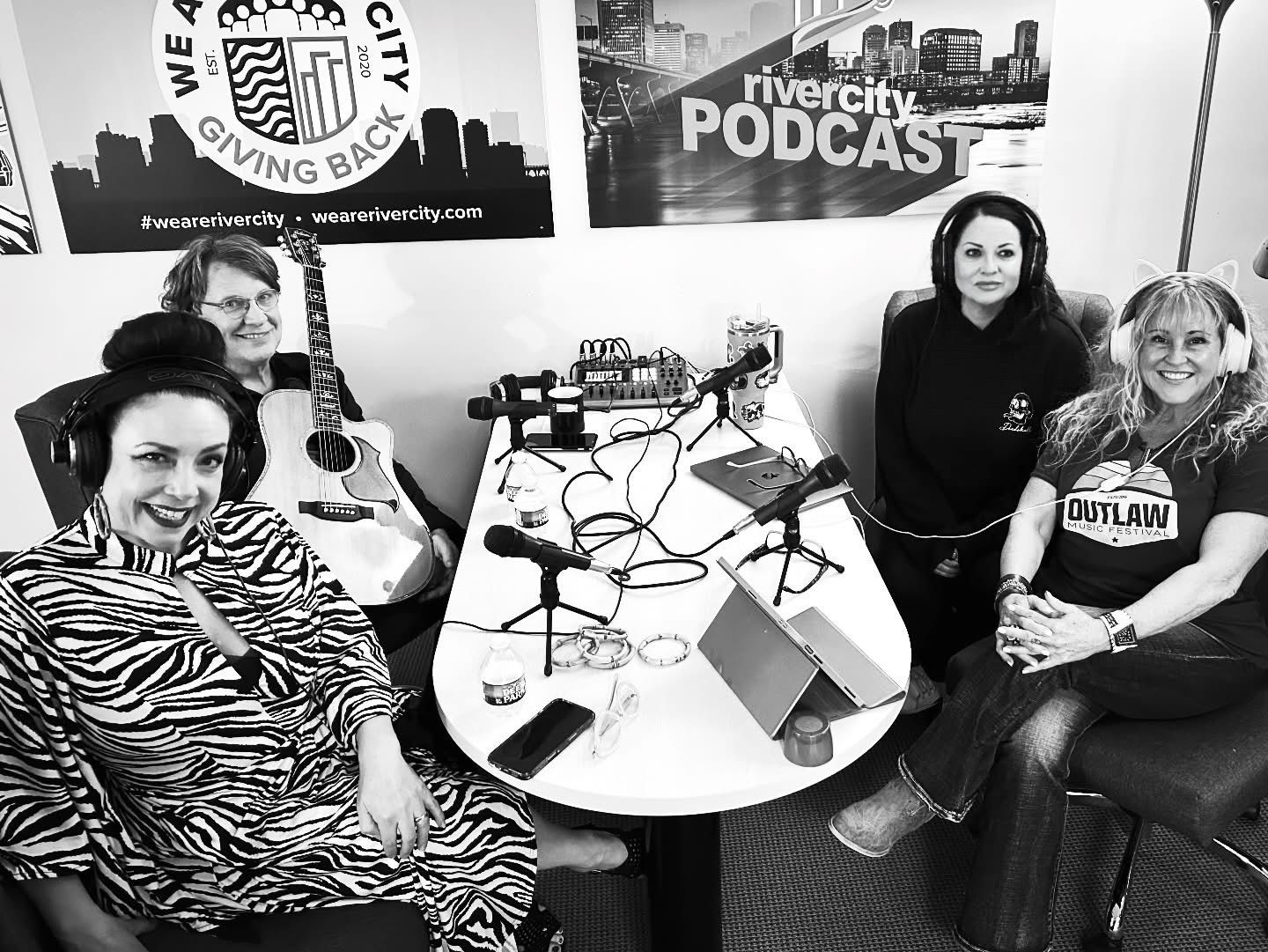 Group of four women seated around a table with microphones, recording a podcast.