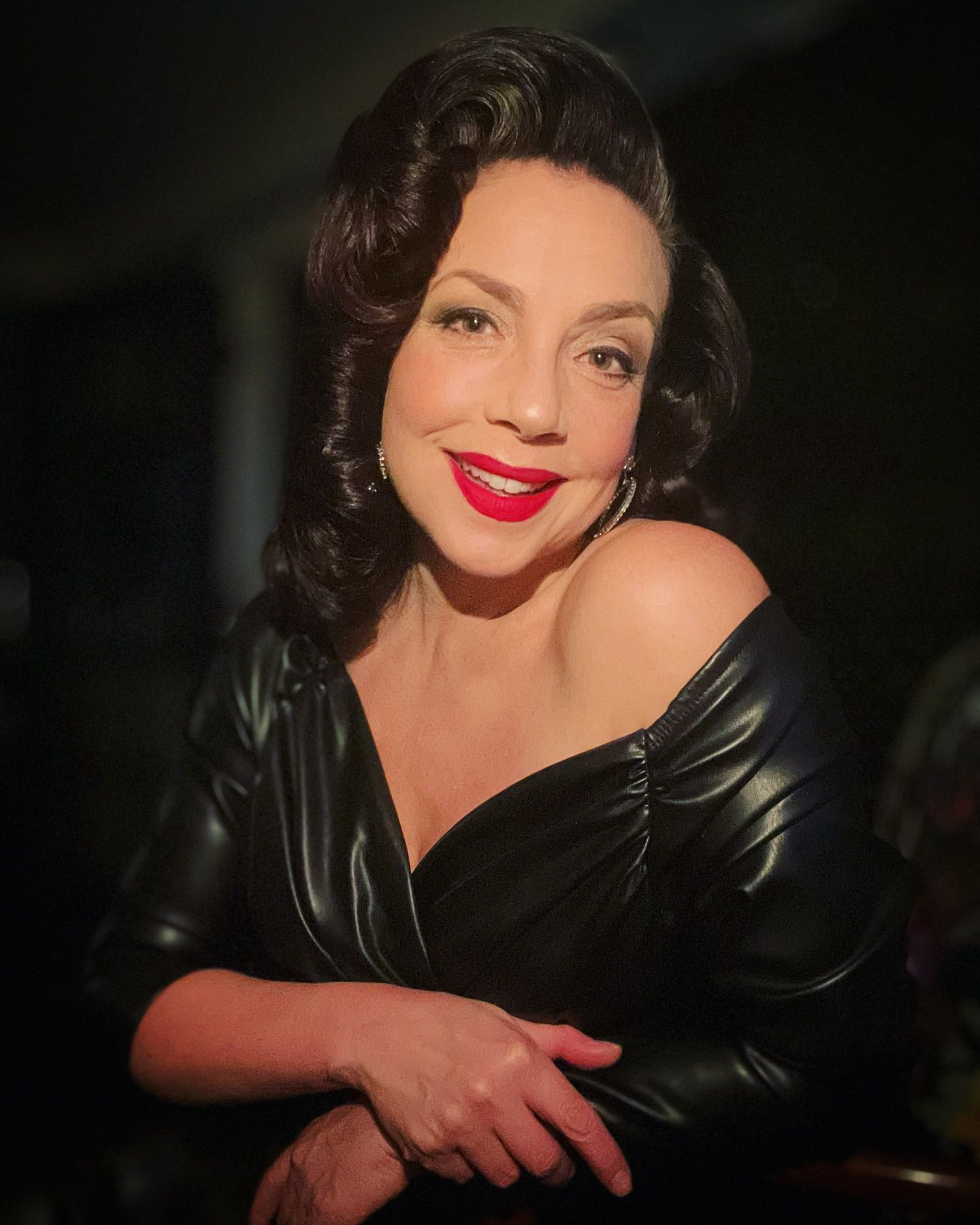 Woman in black off-shoulder top, red lipstick, and retro hairstyle smiling.