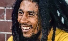 Bob Marley smiling, wearing a yellow shirt and dreadlocks.