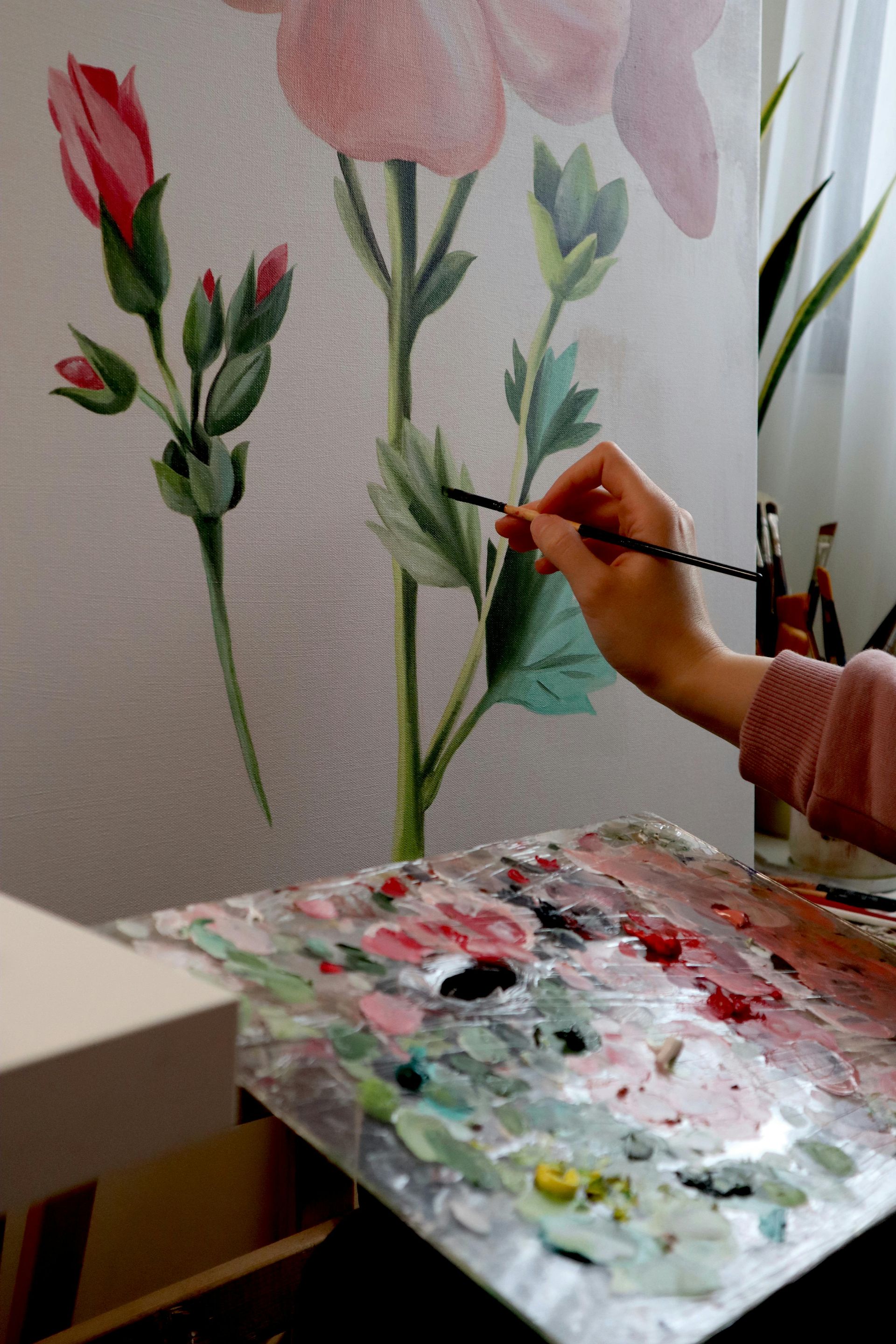A person painting flowers on canvas, using a paintbrush and palette.