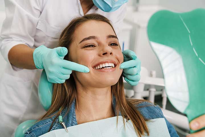  young woman smiling while looking at mirror in dental clinic 