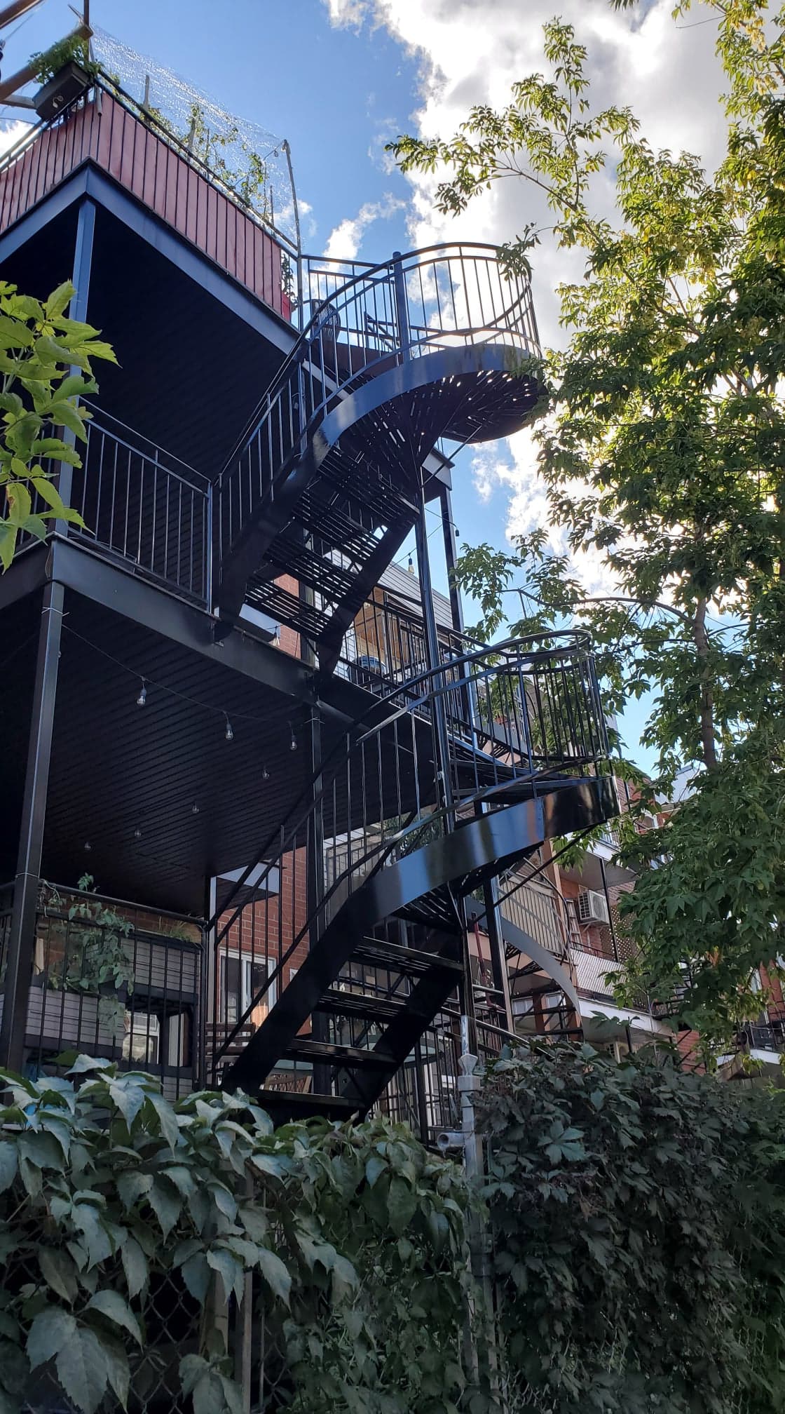 Un escalier menant à un balcon au sommet d'un immeuble entouré d'arbres.