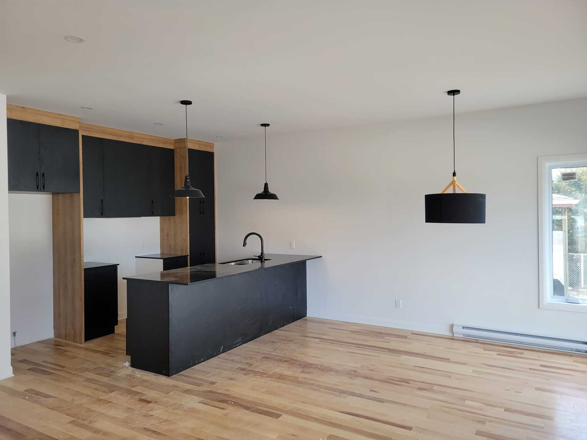 Une cuisine vide avec des armoires noires et du parquet.